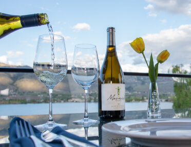Patio table with bottle of wine, two wine glasses and yellow tulips.