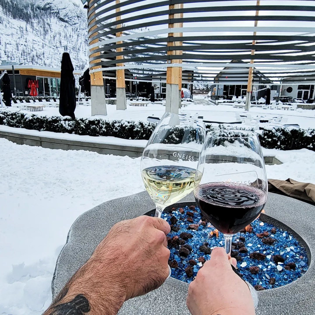Couple holding wine glasses at The District Wine Village in Oliver, BC with a snow scenery.